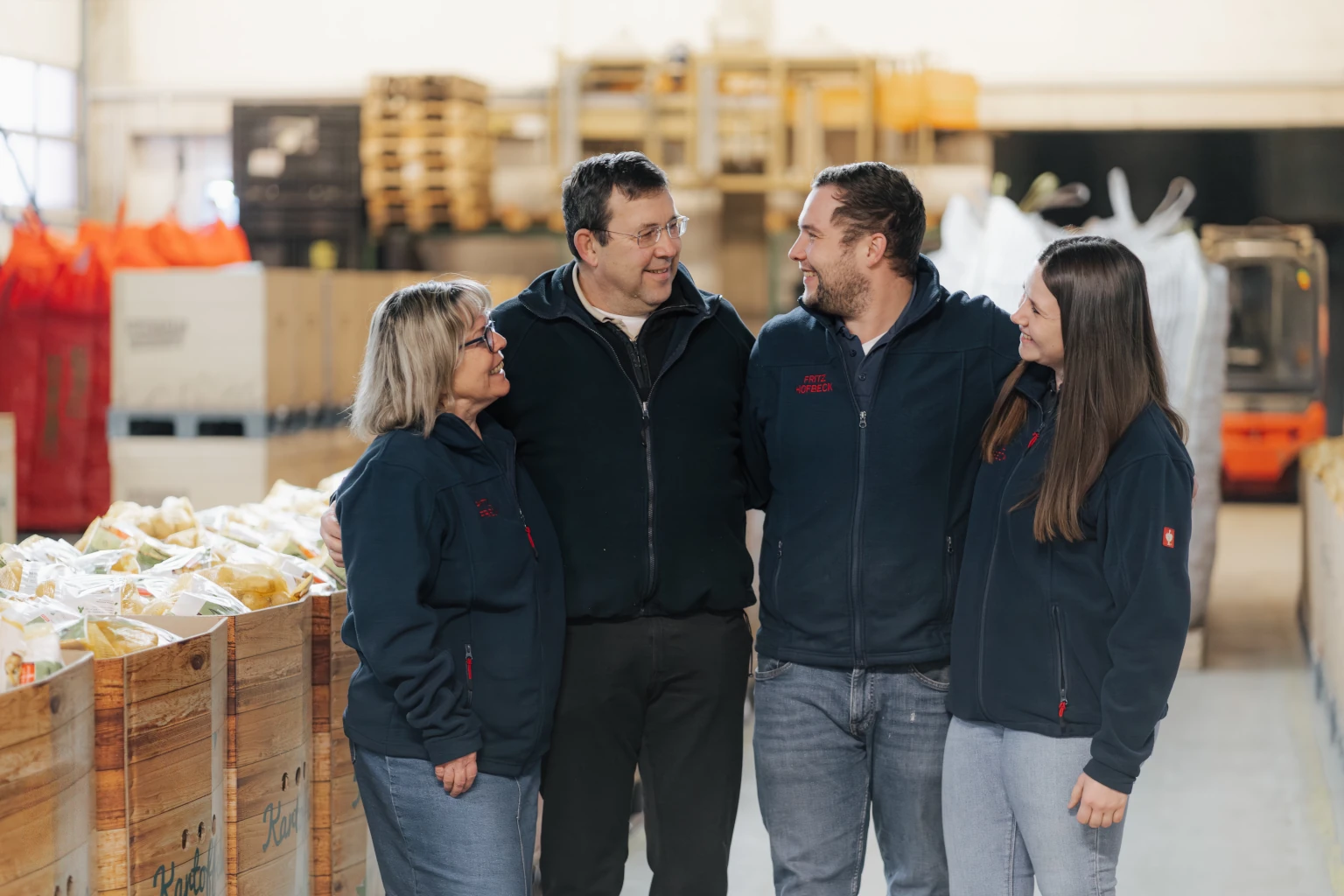 Familie Hofbeck steht gemeinsam im Betrieb von Fritz Hofbeck zwischen verpackten Kartoffeln und Arbeitsbereichen.